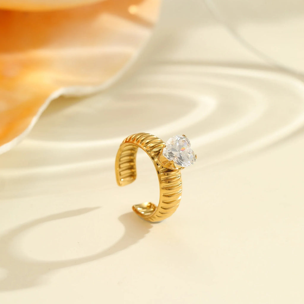Gold-coloured stainless steel ring with an inlaid zircon stone and geometric heart design on an adjustable open mouth band.