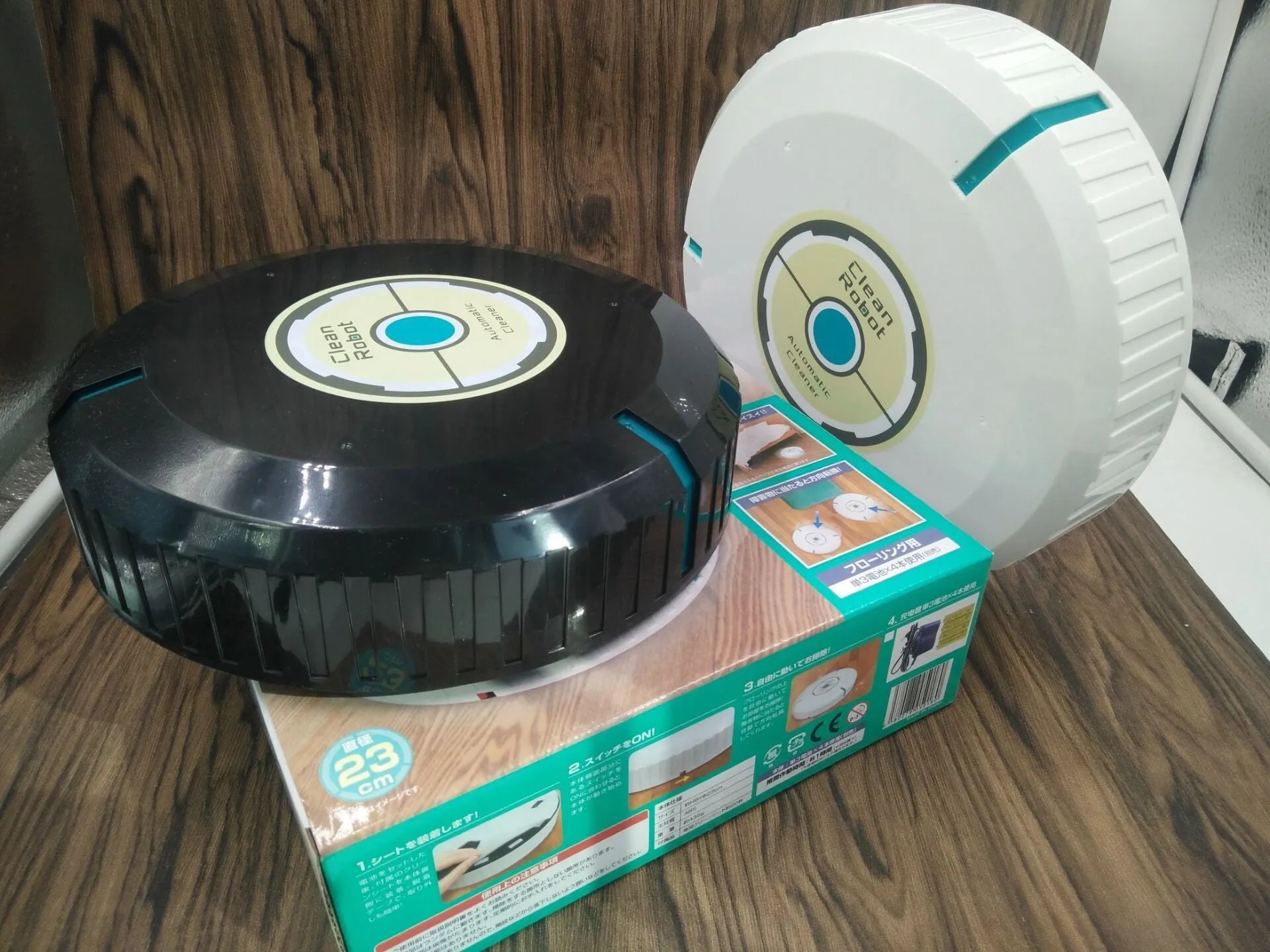 Black or white compact robot vacuum cleaner on a hardwood floor.