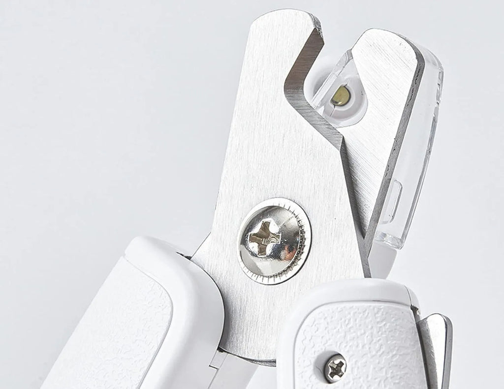 White pet nail clippers with LED light and transparent splash guard open, showing the triangular steel blade.