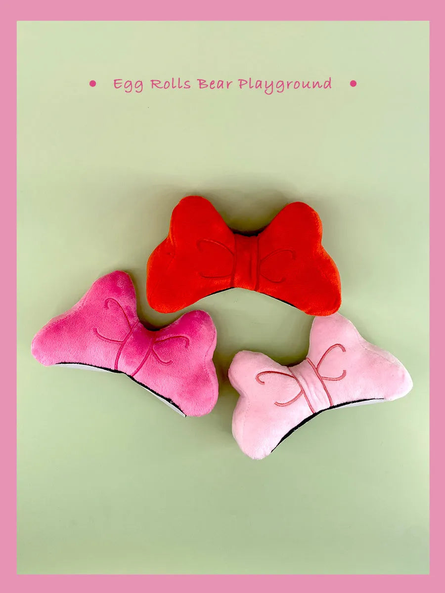 Plush bow tie helmet decoration in red, peach pink, or rose pink colours with elastic strap.