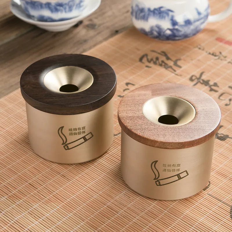 Brass-coloured copper ashtray with a wooden lid featuring a central hole, on a tabletop.