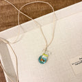 Women's necklace with blue glazed small fish charm pendant on a beige cotton-linen clavicle chain.