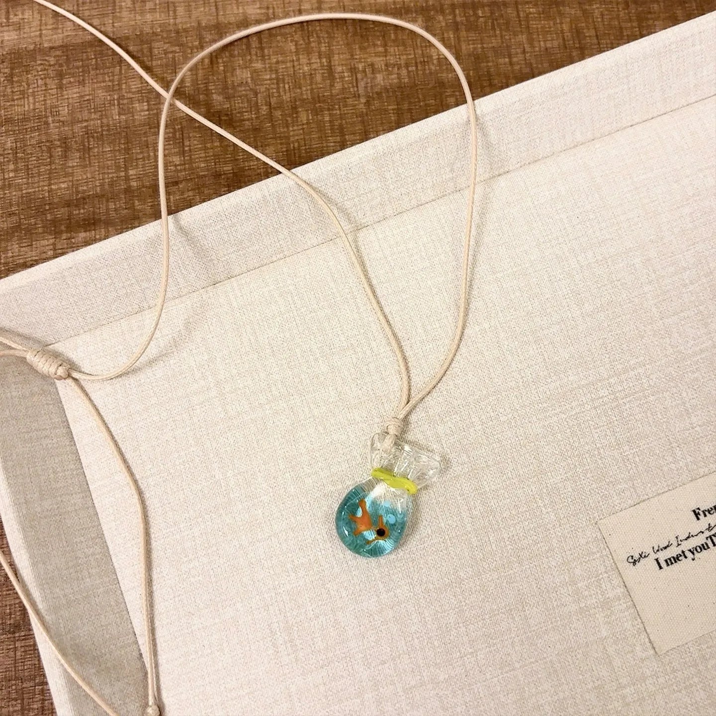 Women's necklace with blue glazed small fish charm pendant on a beige cotton-linen clavicle chain.