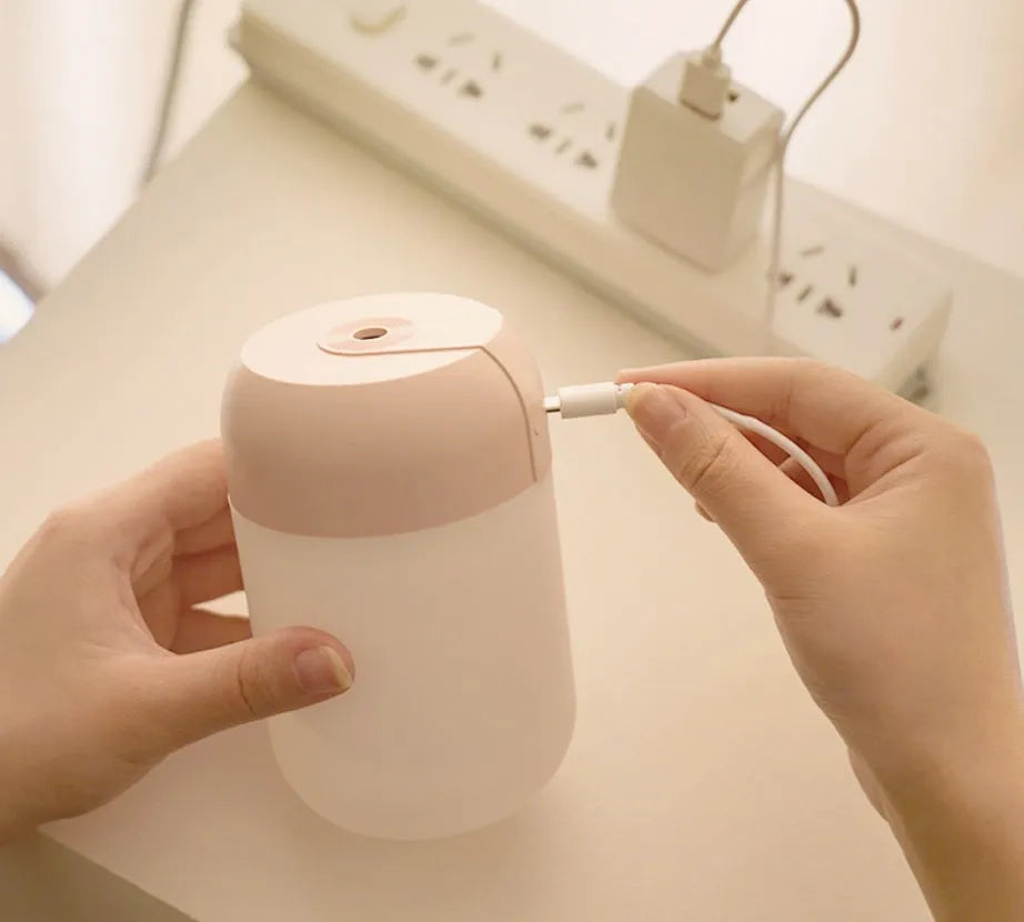 White cylindrical mini USB humidifier on wooden surface with charging cable