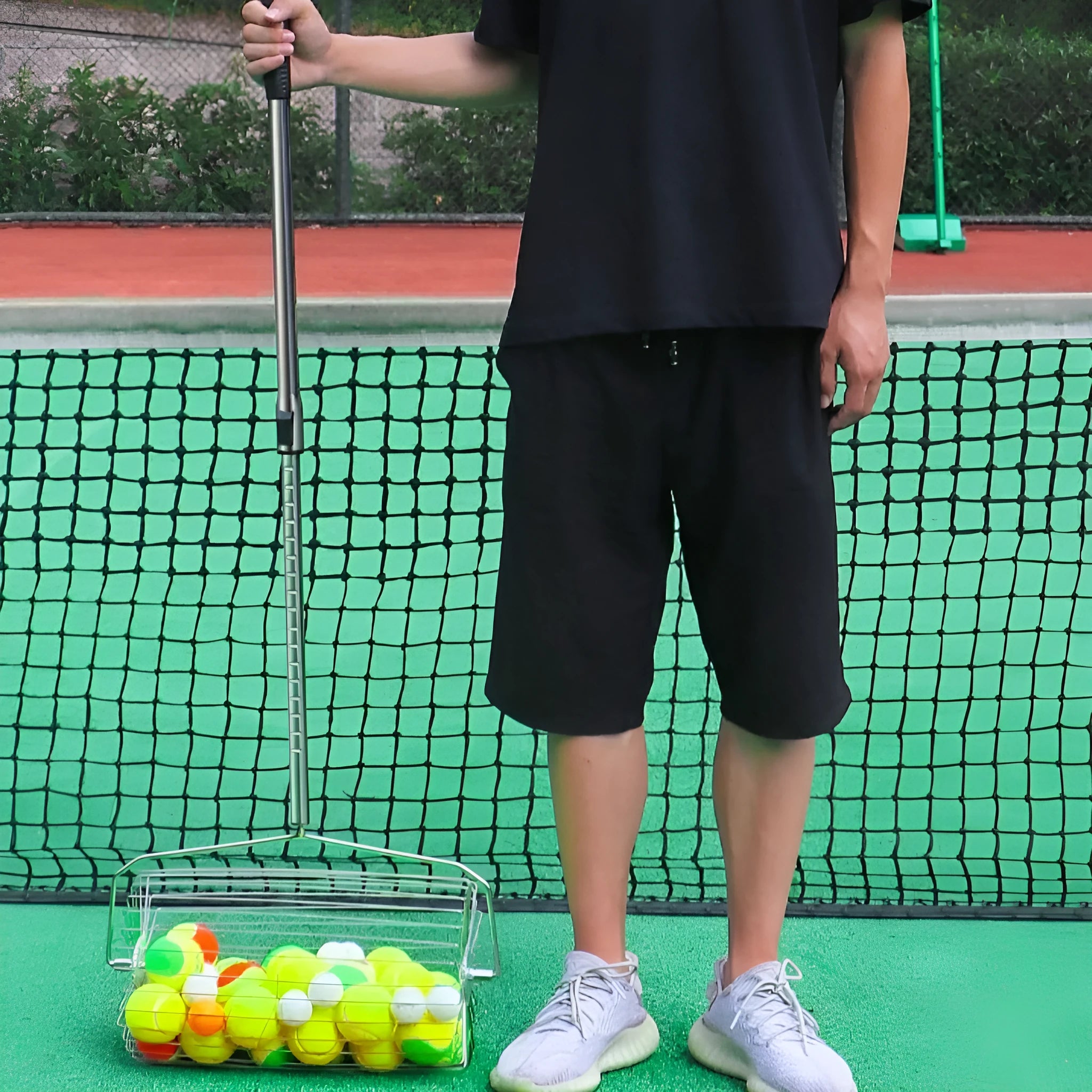 Stainless steel adjustable roller tennis ball picker on a court surface.