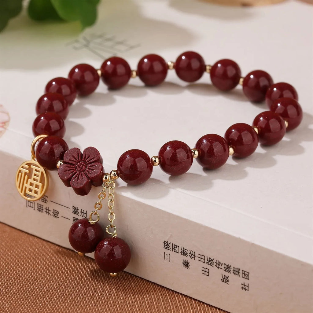 Women's handmade cinnabar bracelet with fu character charm and tassel detail in purple gold sand finish