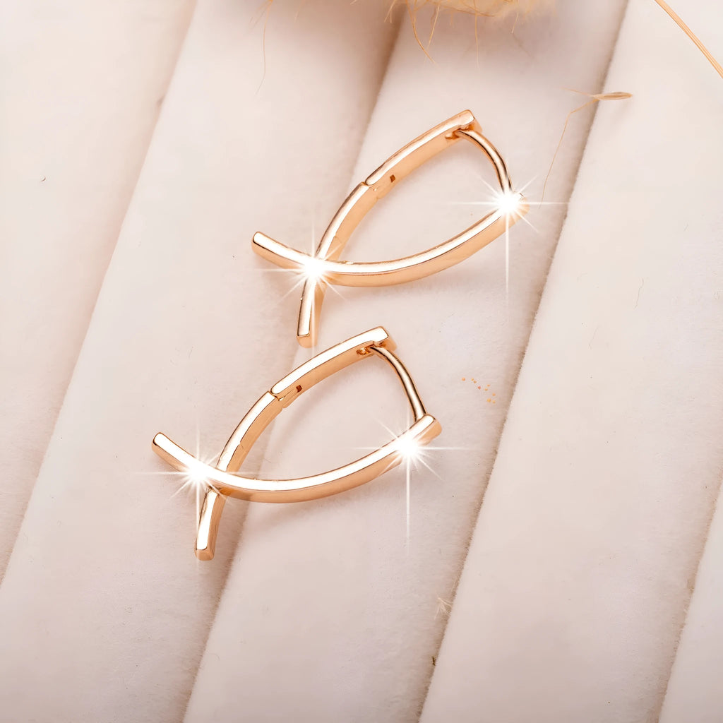 A pair of rose gold cross shaped earrings made from copper on a plain background.