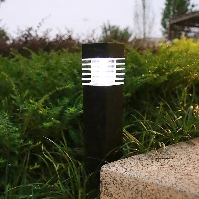 A tall, white, cuboid-shaped solar garden lamp with a ground spike, placed on a lawn.