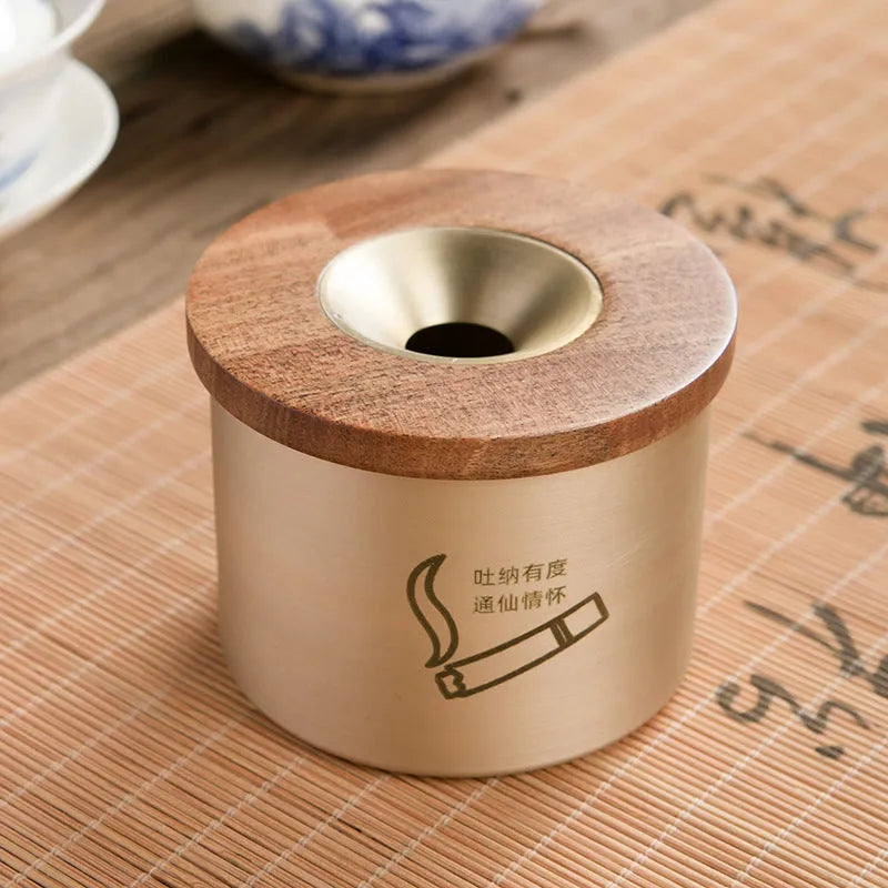 Brass-coloured copper ashtray with a wooden lid featuring a central hole, on a tabletop.