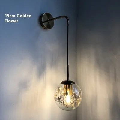 Modern glass wall lamp in golden flower finish mounted beside a bed.