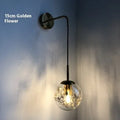 Modern glass wall lamp in golden flower finish mounted beside a bed.