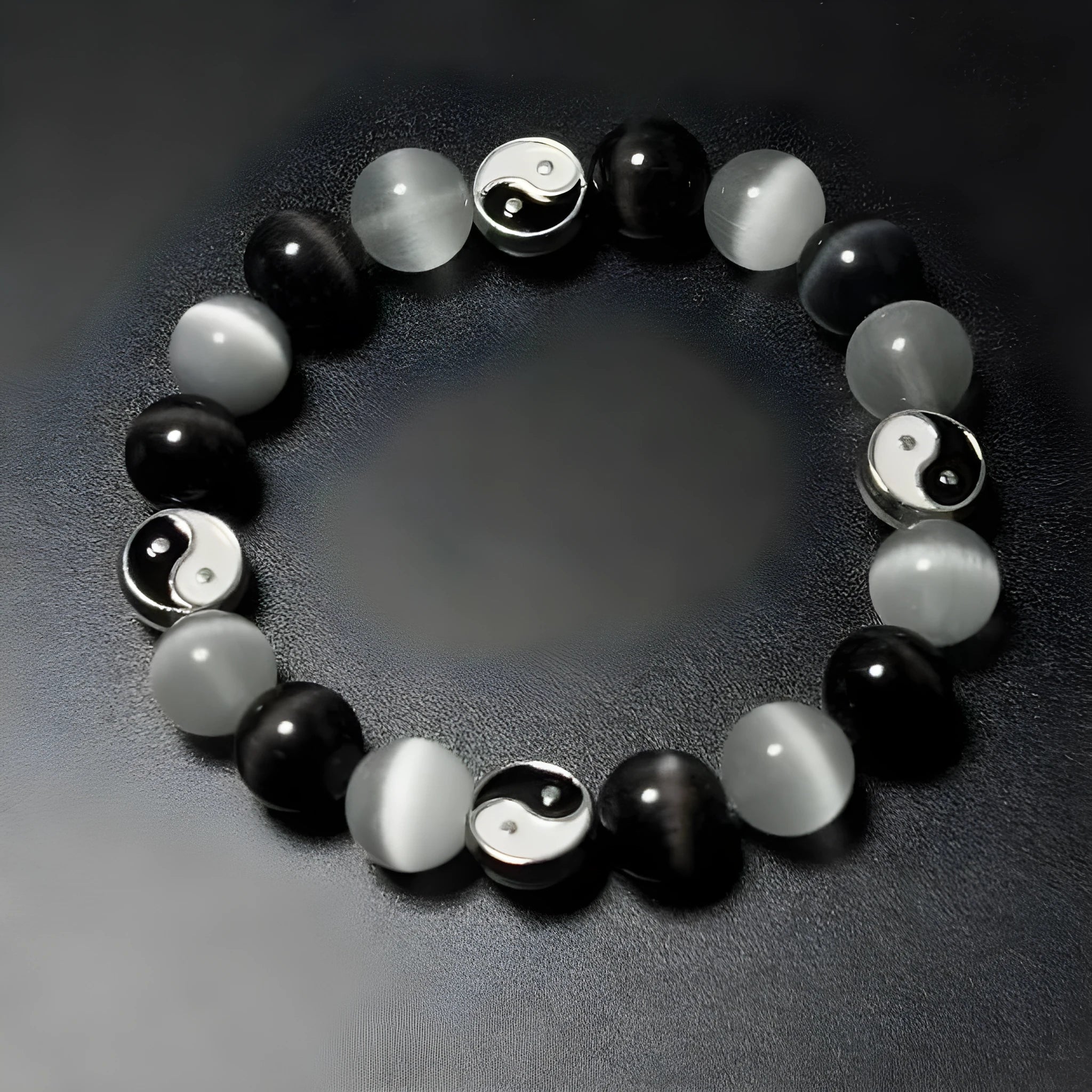 A polished black agate opal beaded bracelet with an ornamental Tai Chi symbol, shown on a wrist.