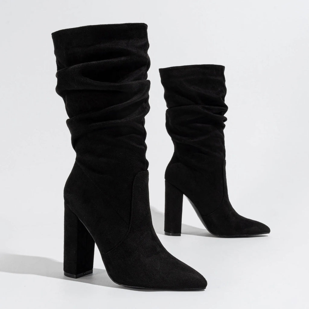 Women's black suede high heel boots with a chunky heel and pointed toe, shown on a model.