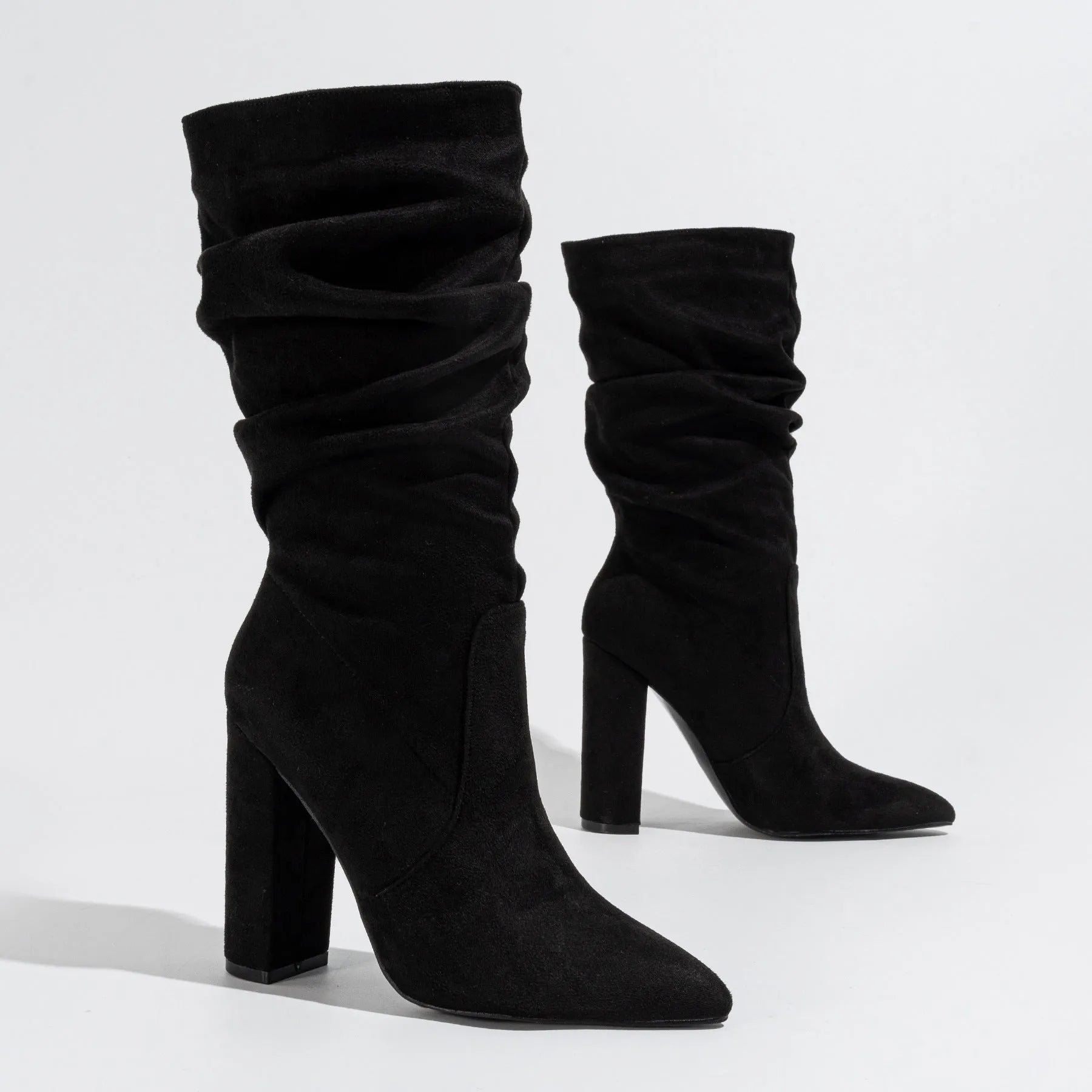 Women's black suede high heel boots with a chunky heel and pointed toe, shown on a model.