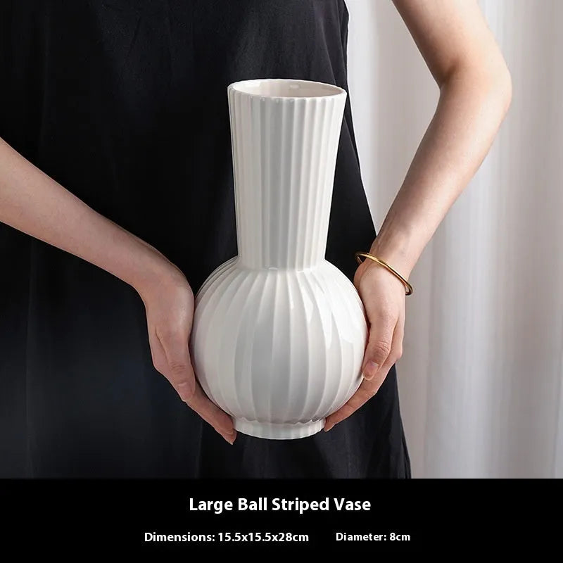 White ceramic ball vase with vertical stripes on a wooden table, with optional artificial purple orchid stems.