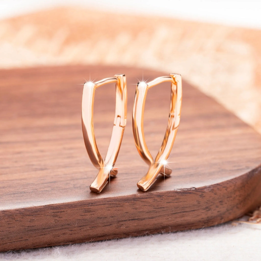 A pair of rose gold cross shaped earrings made from copper on a plain background.