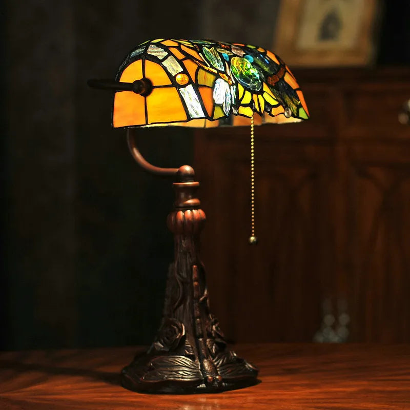 Tiffany-style table lamp with coloured glass shade and resin base on a wooden desk.