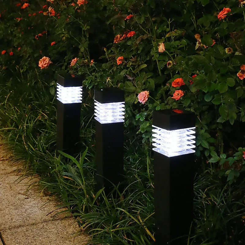 A tall, white, cuboid-shaped solar garden lamp with a ground spike, placed on a lawn.