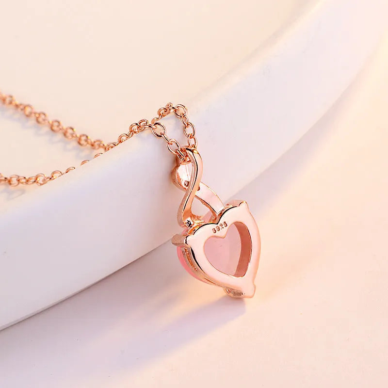 Women's pink heart crystal pendant necklace with rose gold cross chain on copper.