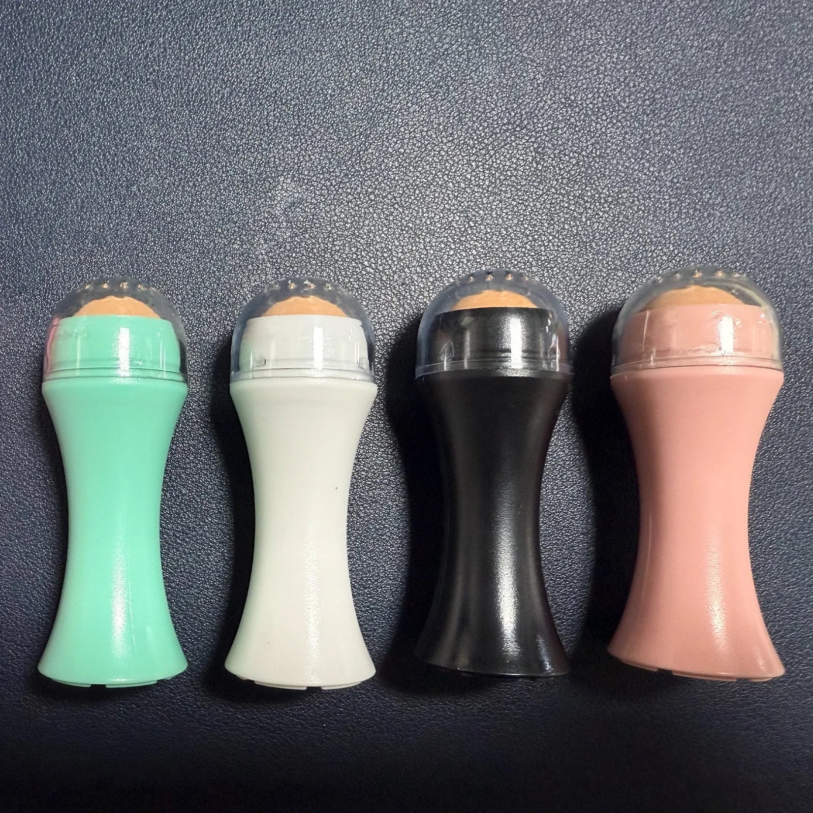 Volcanic stone portable roller for oily skin in black, green, pink or white on a grey background.