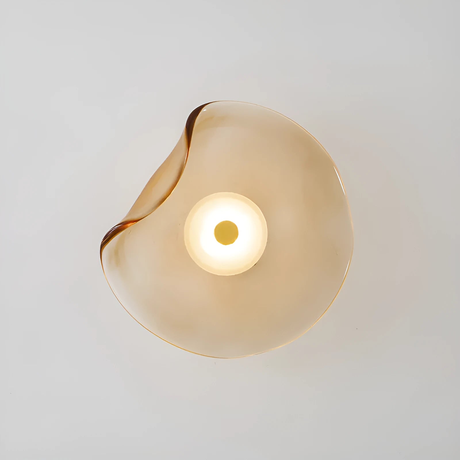 Round glass wall lamp in cognac colour mounted beside bed with warm lighting