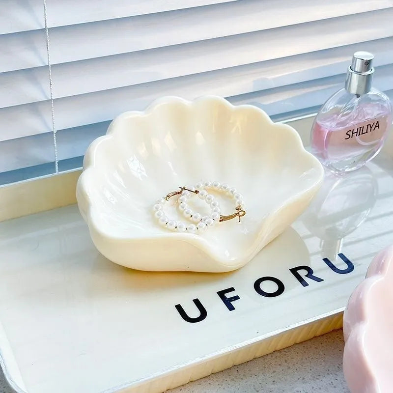 White shell-shaped plastic soap dish for bathroom counter next to pink version.