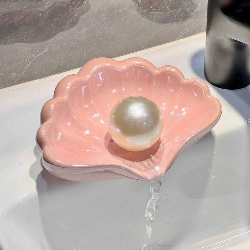 White shell-shaped plastic soap dish for bathroom counter next to pink version.