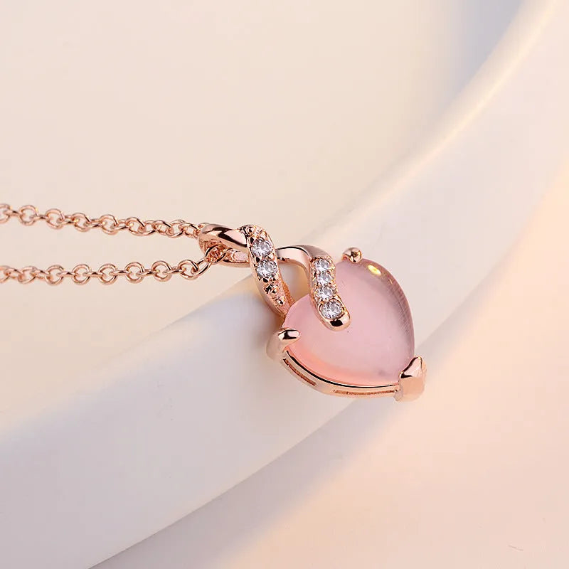 Women's pink heart crystal pendant necklace with rose gold cross chain on copper.