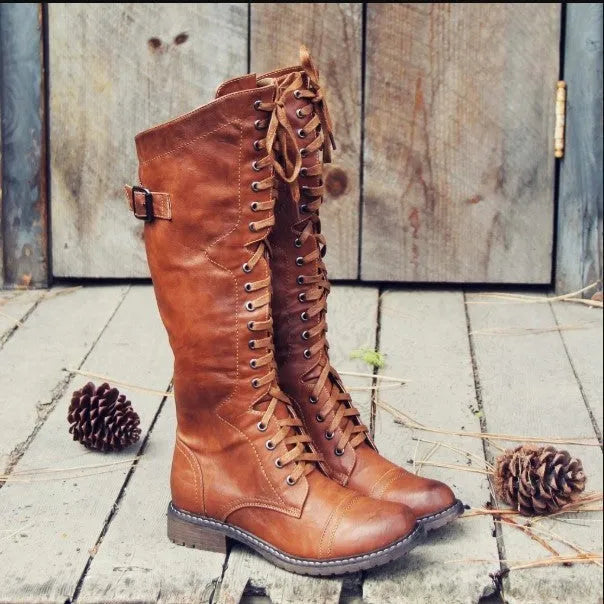 Women's black artificial PU knight boots with cross strap detail on ankle.