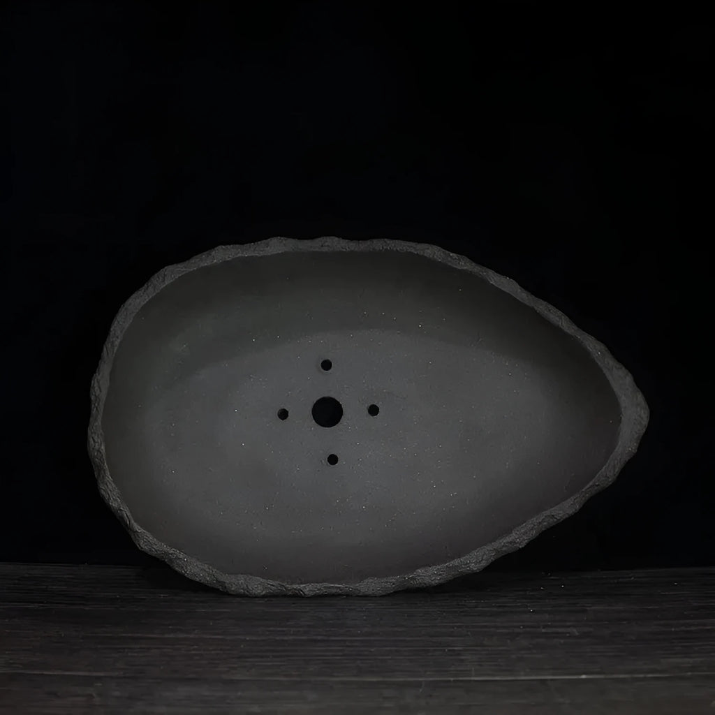 Handmade purple clay flower pot with unique shape displayed on floor with green plant