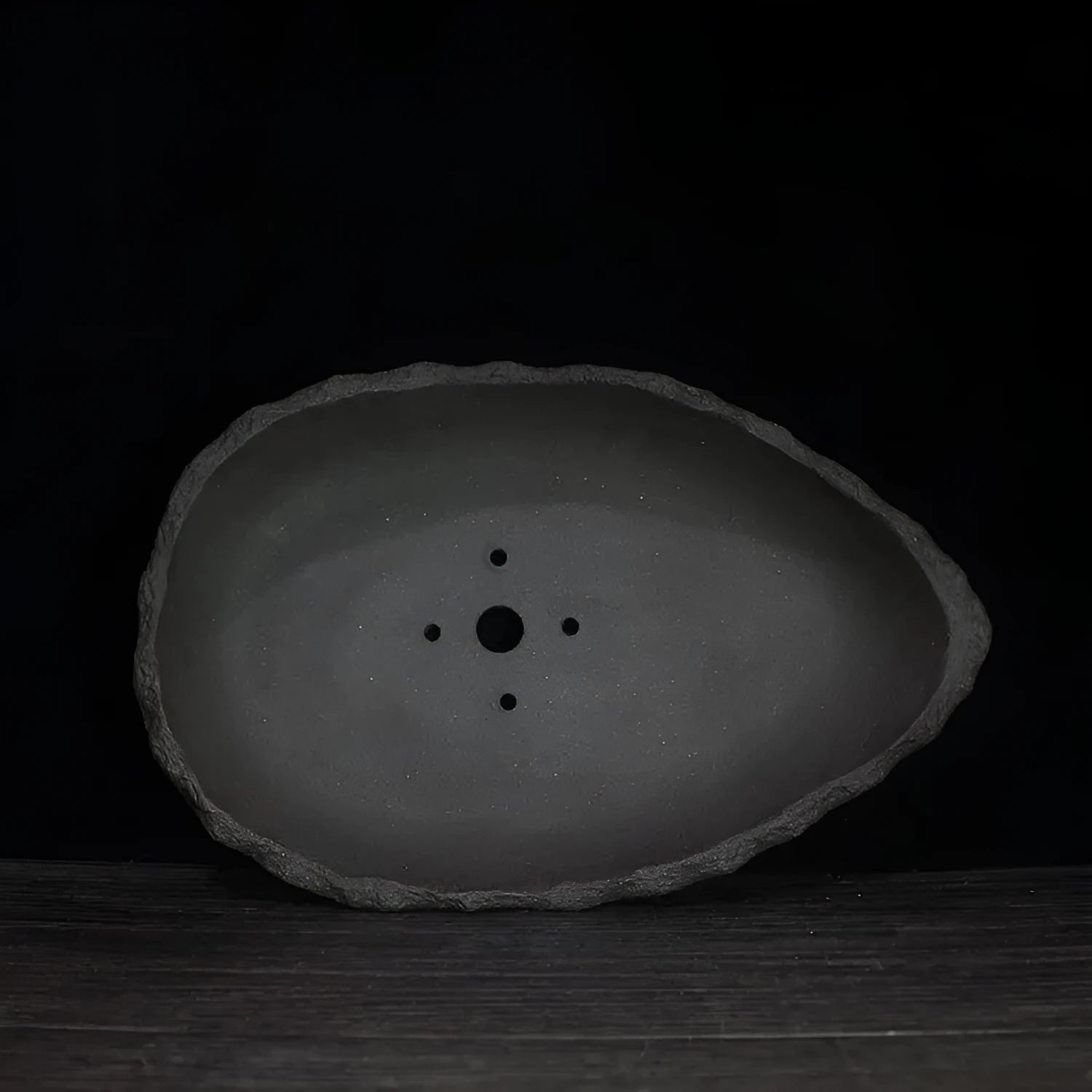 Handmade purple clay flower pot with unique shape displayed on floor with green plant