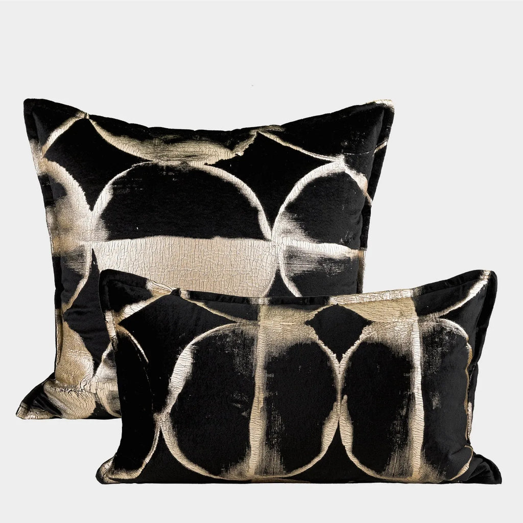Black and gold abstract patterned flannel decorative cushion on a grey sofa.