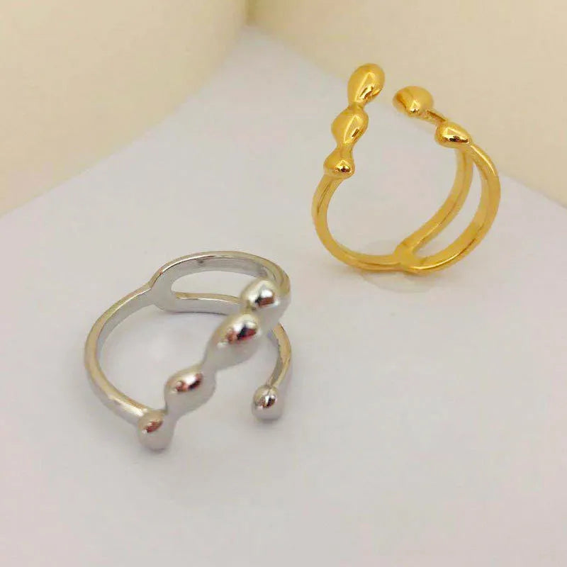 Gold and silver coloured brass opening ring with spherical design on a white background.