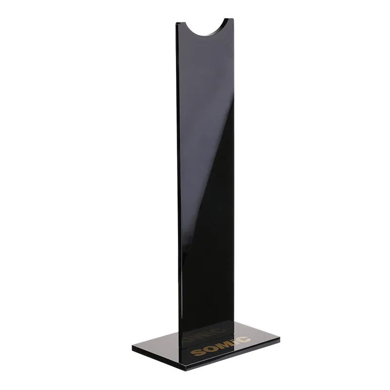 Black detachable head-mounted gaming headset stand with a silicone base on a wooden desk.