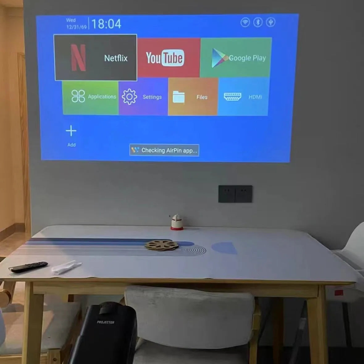 White home projector with carrying handle on a table, set up for wireless gaming projection.