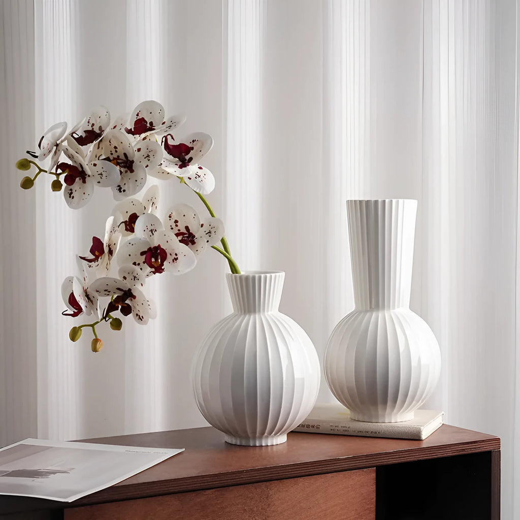 White ceramic ball vase with vertical stripes on a wooden table, with optional artificial purple orchid stems.