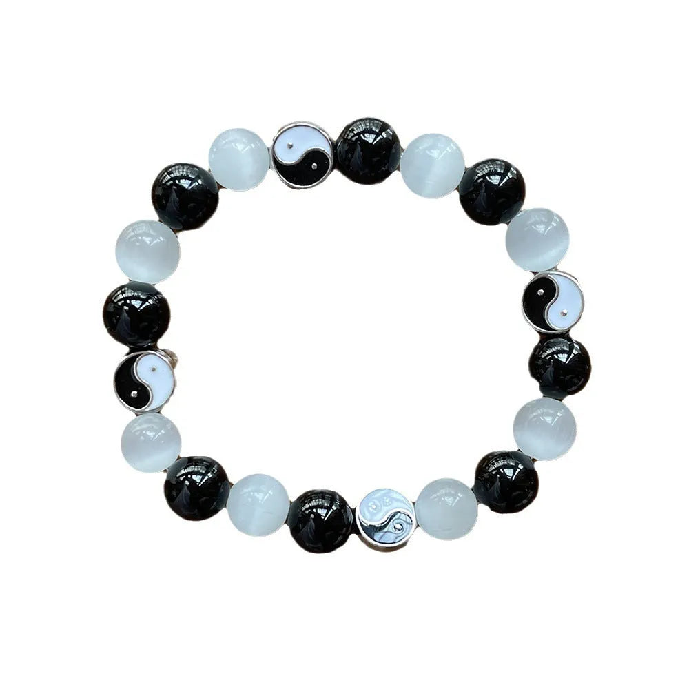 A polished black agate opal beaded bracelet with an ornamental Tai Chi symbol, shown on a wrist.
