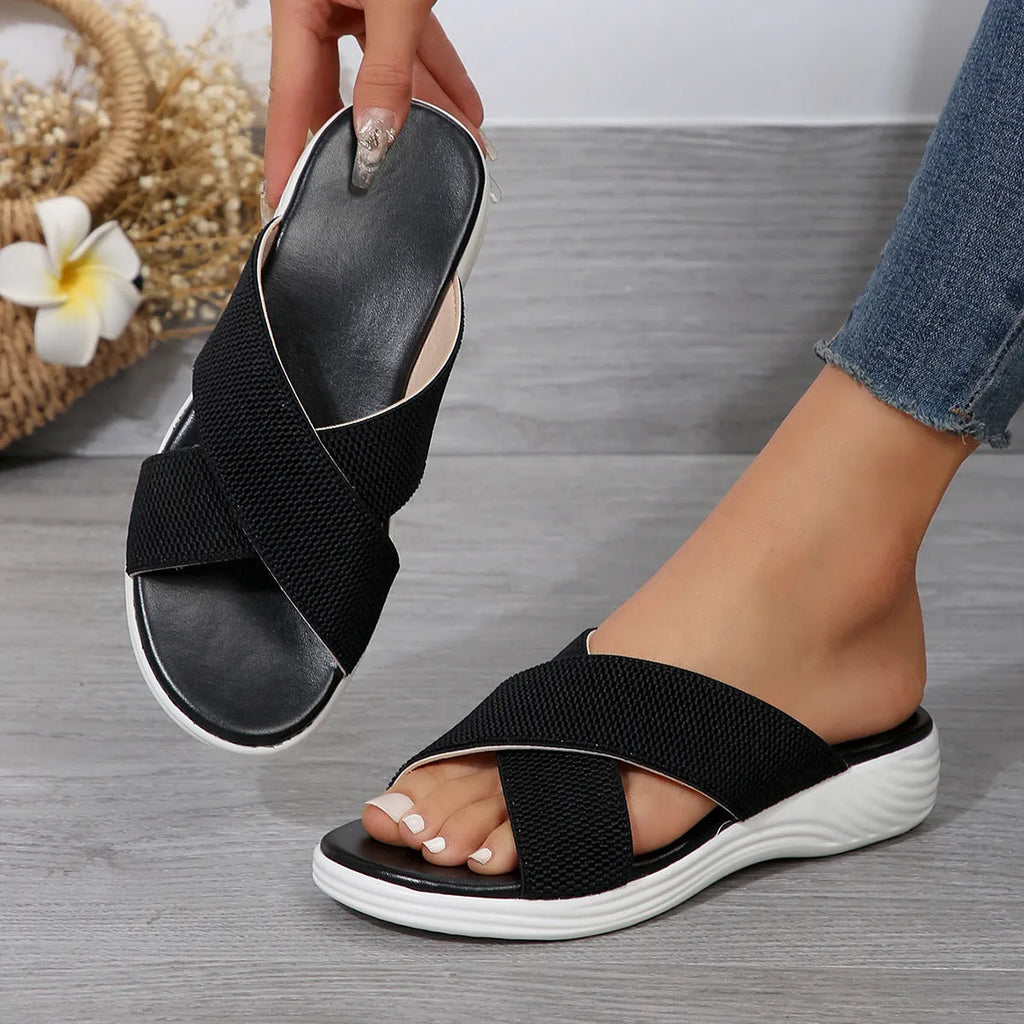 Black women's wedge slipper with a cross strap and open peep-toe on a thick rubber sole.