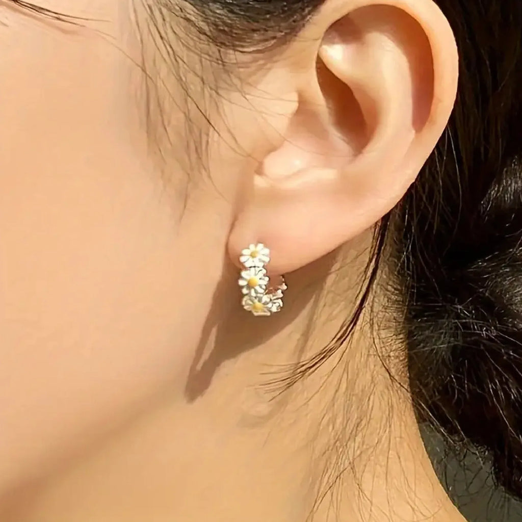 A pair of white daisy flower ring earrings with a gemstone inlay, shown on a model or display.