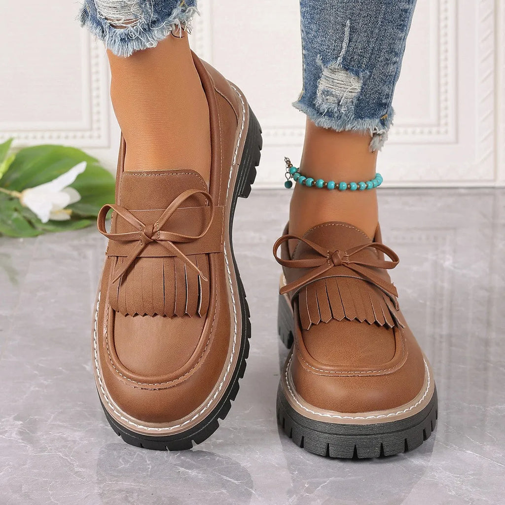 Black women's loafers with a tassel and bowknot decoration on the front.