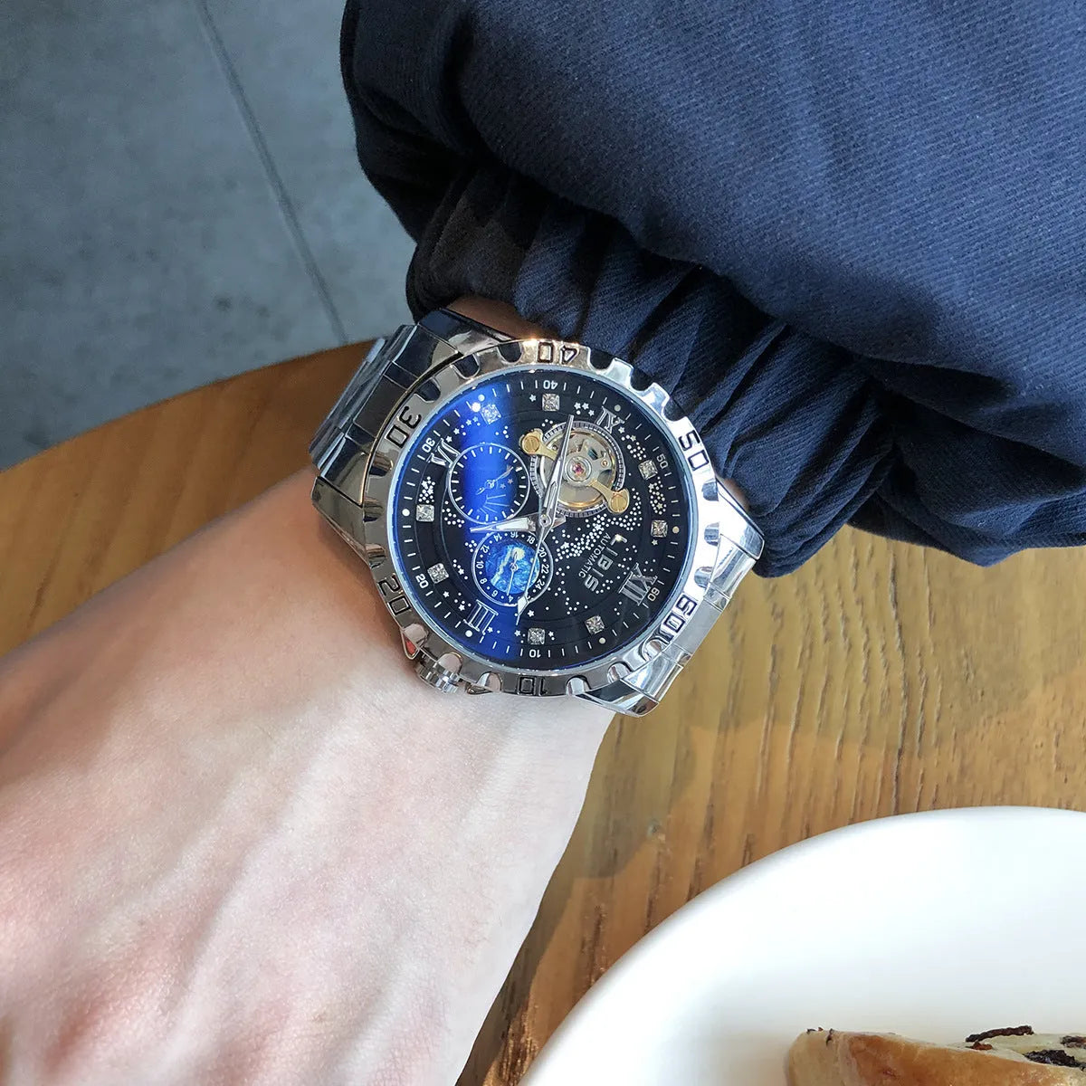 Men's silver automatic watch with black starry dial and leather strap showing luminous hands