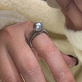 Copper geometric open ring with a black pearl, shown on a woman's index finger.