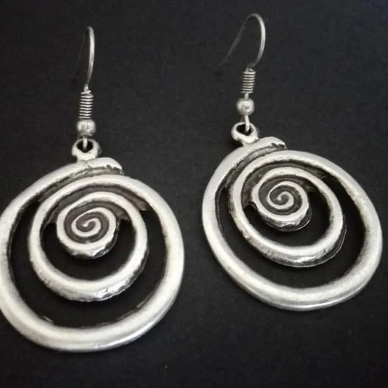Close-up of a pair of silver geometric spiral earrings with a distressed vintage finish.
