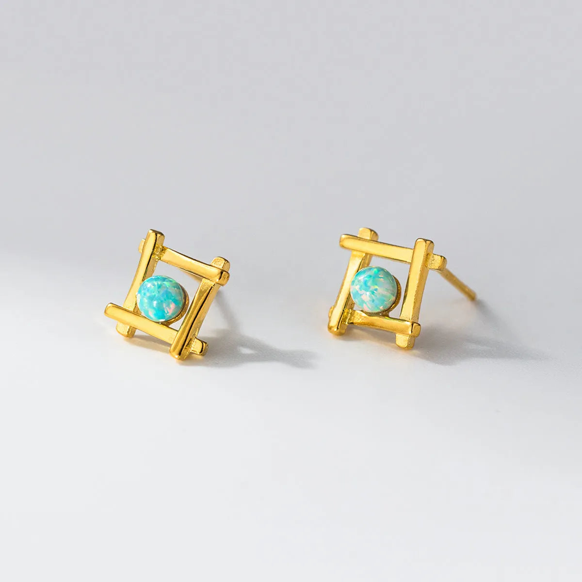 Geometric cross-shaped quadrangle stud earrings in sterling silver, shown in both silver and gold-plated finishes.