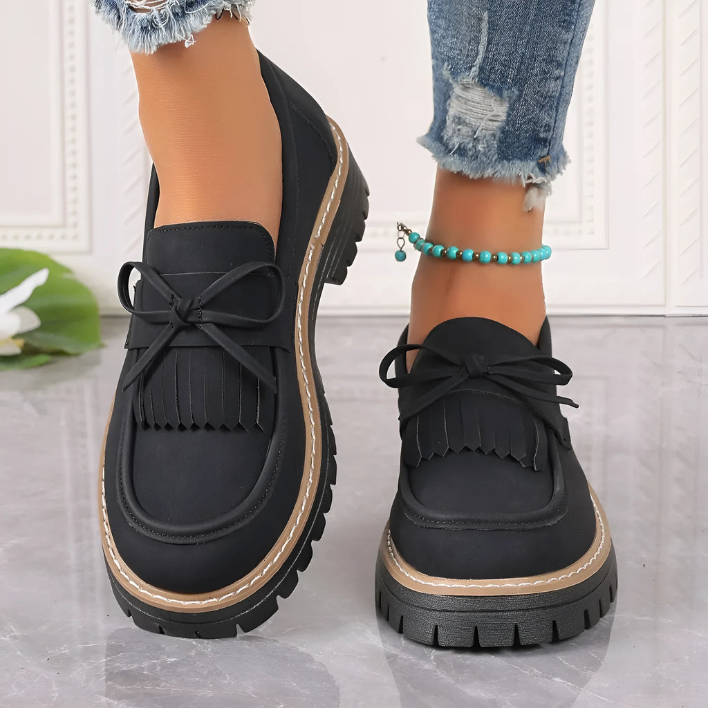 Black women's loafers with a tassel and bowknot decoration on the front.