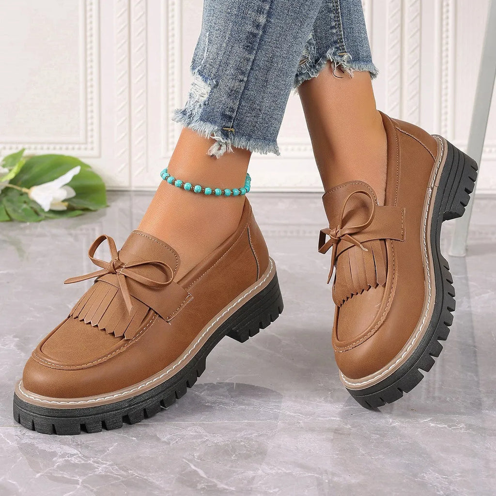 Black women's loafers with a tassel and bowknot decoration on the front.