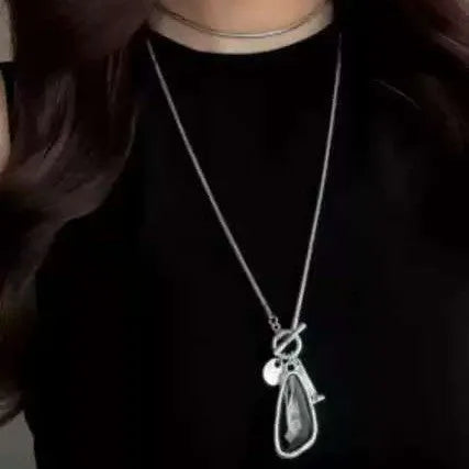 Geometric plaid pendant on a long snake chain necklace layered over a jumper.
