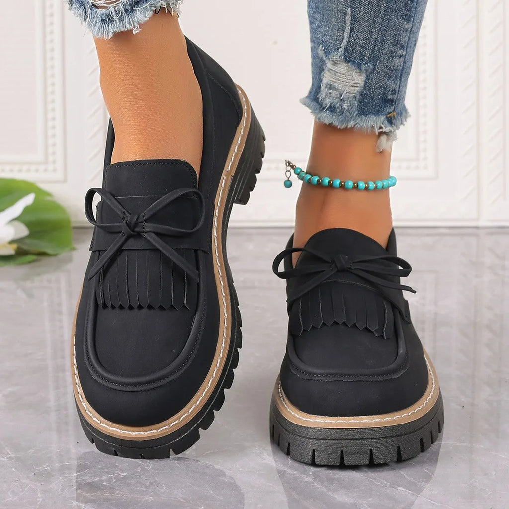 Black women's loafers with a tassel and bowknot decoration on the front.