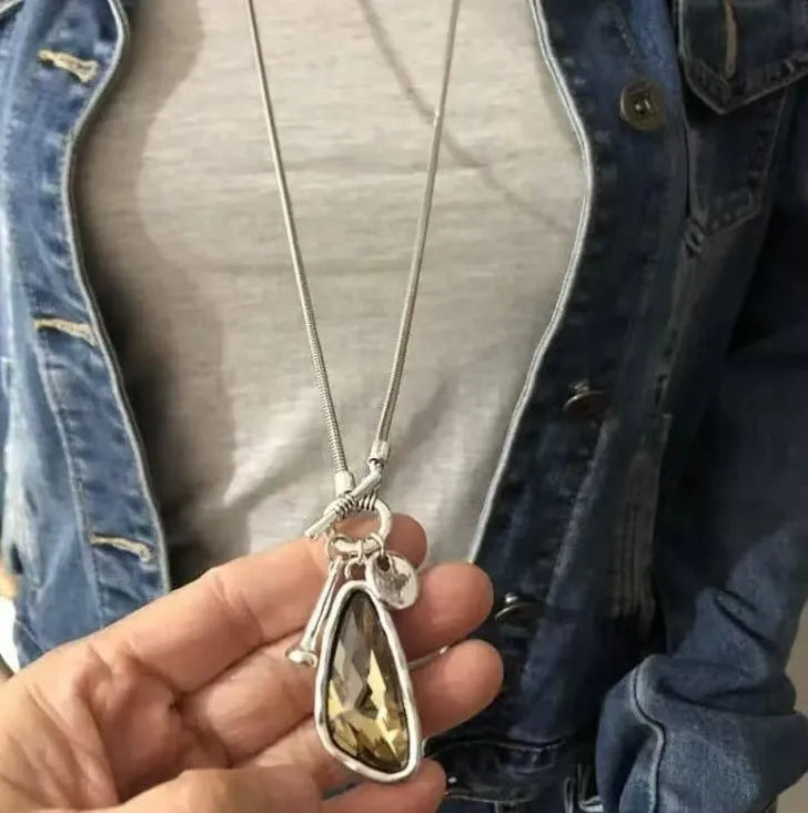 Geometric plaid pendant on a long snake chain necklace layered over a jumper.