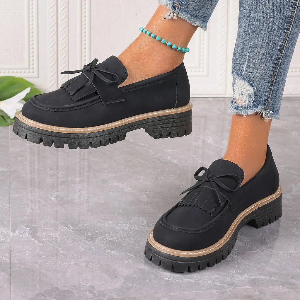 Black women's loafers with a tassel and bowknot decoration on the front.